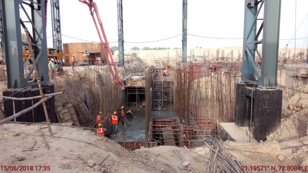 Construction site with workers and heavy machinery, showing the foundation work including steel reinforcements and concrete pouring.