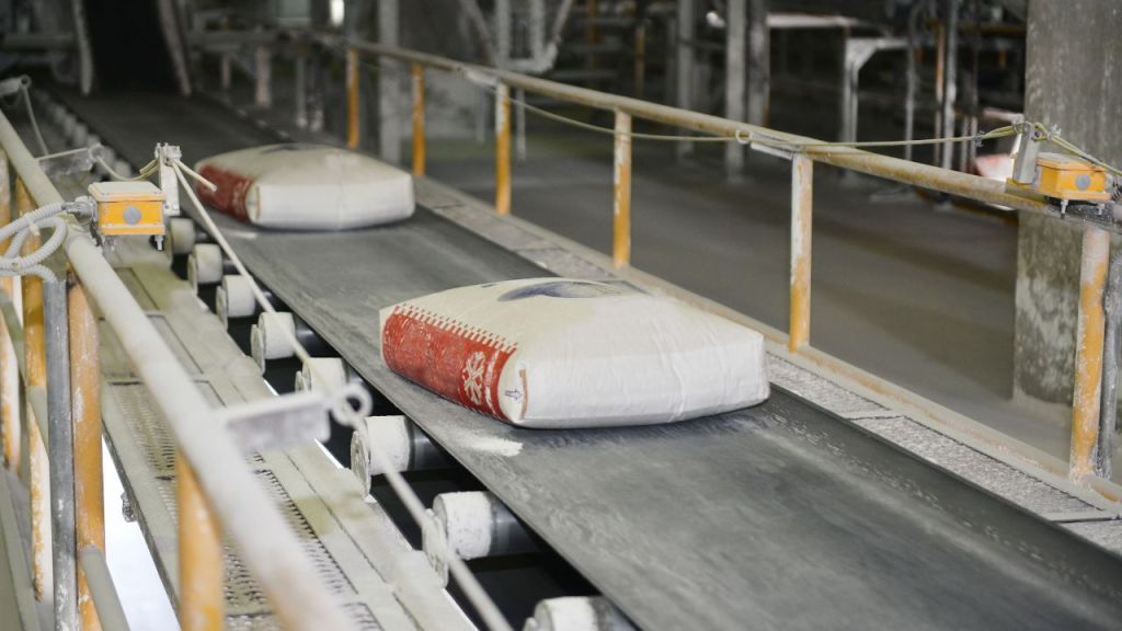 Bags of cement moving along a conveyor belt in a manufacturing facility.