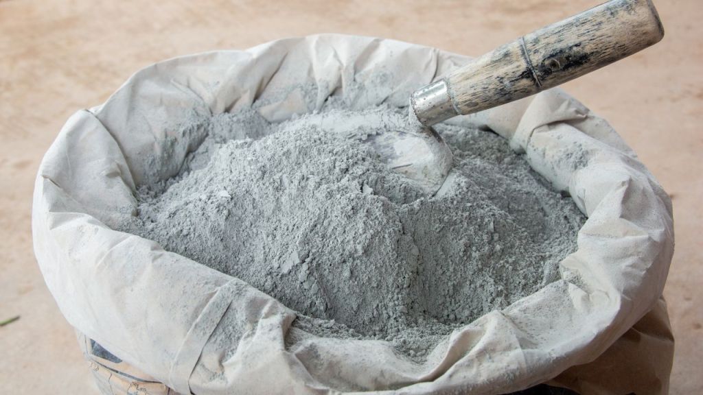 A bag of gray cement powder with a trowel resting on the surface, showcasing its fine texture and color.