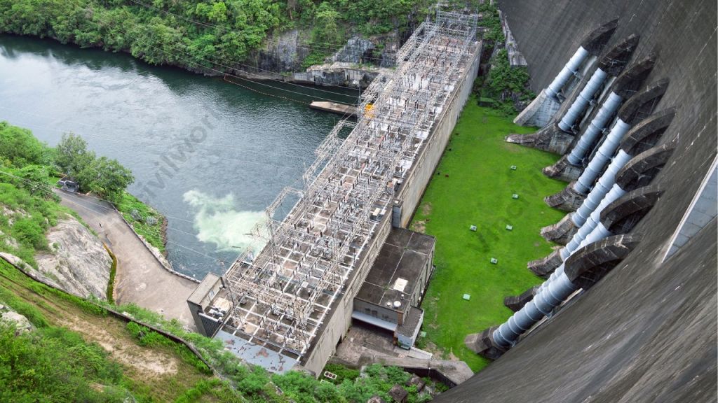 Aerial view of a dam and power generation facility, showcasing the water reservoir, power lines, and surrounding greenery.