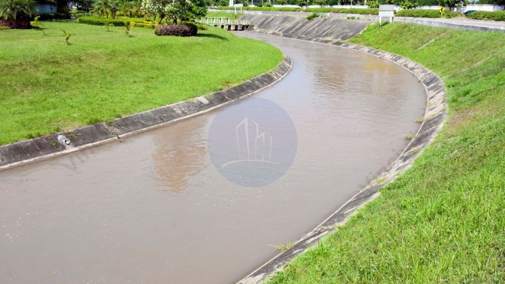 A curved canal filled with water, bordered by green grass and plants, illustrating a flow irrigation system.
