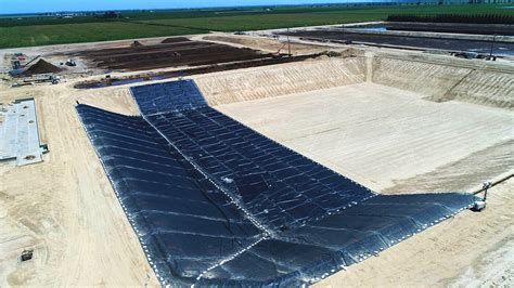 A large geomembrane liner deployed in a dug-out containment area, surrounded by construction materials and equipment, showcasing its application in environmental engineering.
