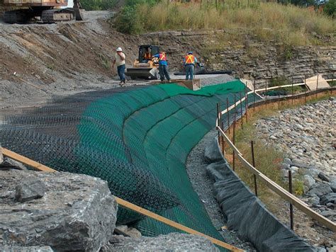 Workers installing geogrids and erosion control measures on a slope during a civil engineering project.