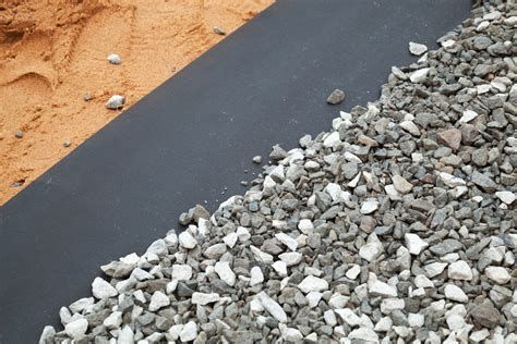 A close-up image showing a black geosynthetic membrane laid between two types of soil, with gravel on one side and sand on the other, illustrating the separation function in civil engineering applications.