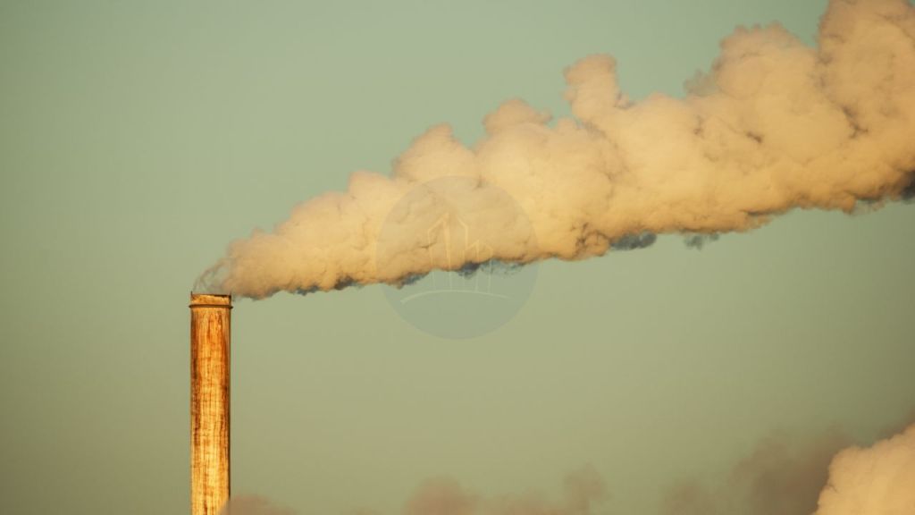 A smoke stack emitting a plume of white smoke against a clear sky, illustrating air pollution in industrial environments.
