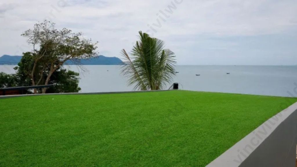 A lush green rooftop lawn overlooking a calm sea with distant mountains and a few boats in the water.