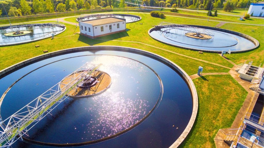 An aerial view of a wastewater treatment facility featuring circular sedimentation tanks, a treatment building, and surrounding green space.