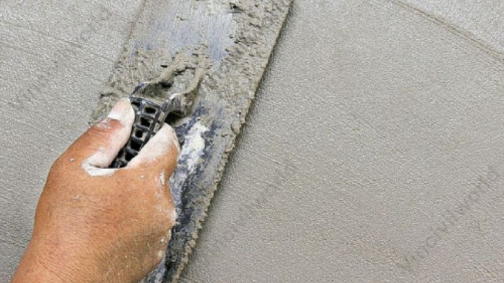 A close-up of a hand applying plaster to a wall using a trowel, showcasing a smooth and even surface being created.