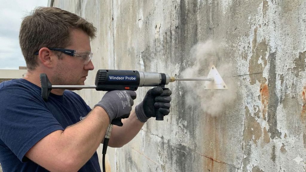A professional using a Windsor Probe device to conduct non-destructive testing on a concrete wall, assessing its strength and quality without causing damage.