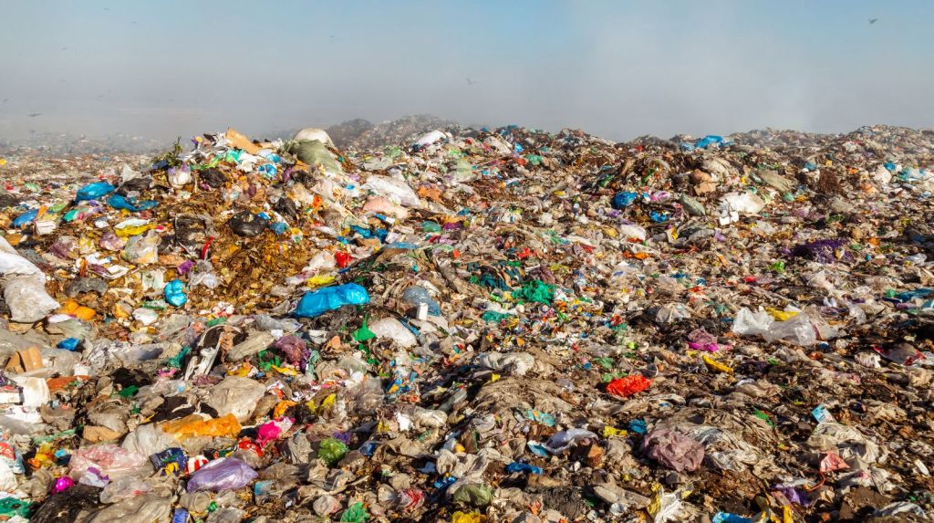 A sprawling landfill site filled with various types of waste, including plastic bags and debris, under a clear sky.