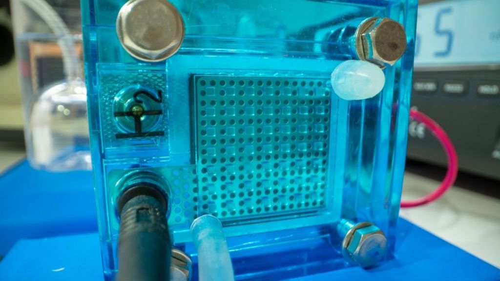 Close-up view of a hydrogen fuel cell assembly, showcasing the transparent casing and inlet connections for hydrogen and oxygen.