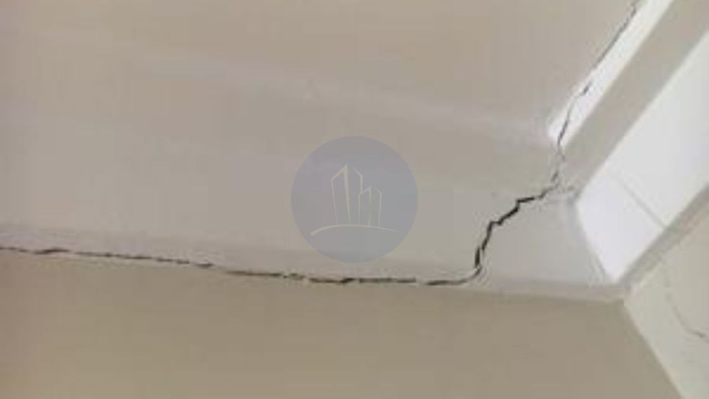 A close-up view of a cracked ceiling, showing a prominent diagonal crack where the ceiling meets the wall, indicating poor workman ship