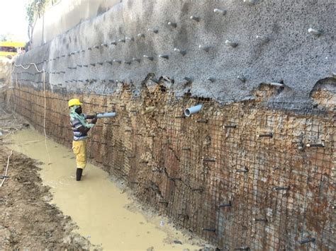 Construction worker applying shotcrete to a soil-nailing wall structure for slope stabilization.